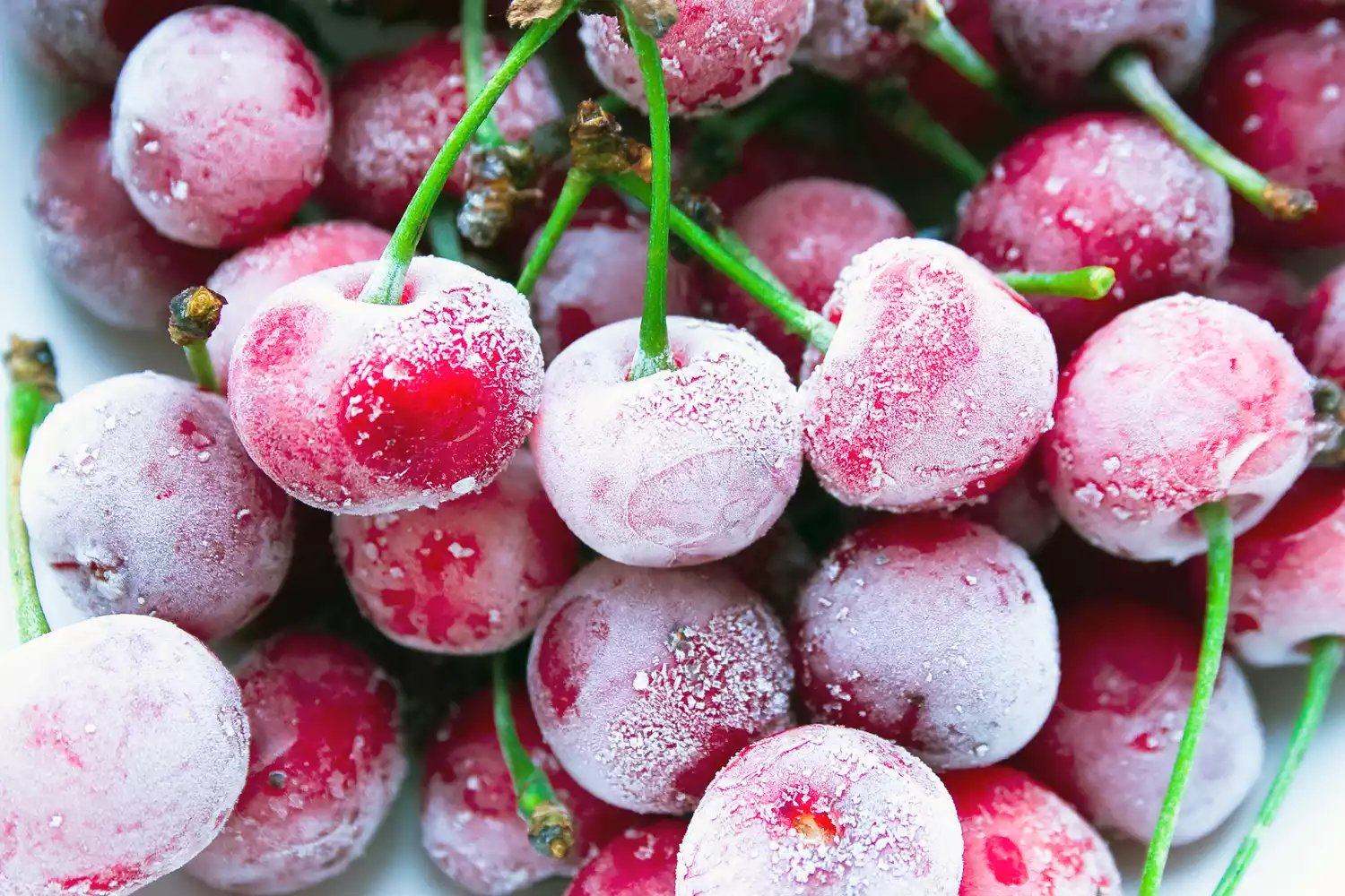 Frozen ripe cherry berries lie on a white surface covered with hoarfrost